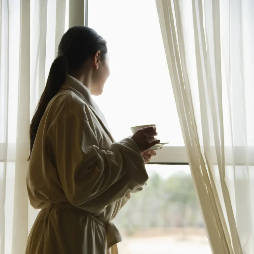 A woman stands tall, sunlight on her face, symbolizing hope and strength after escaping abuse